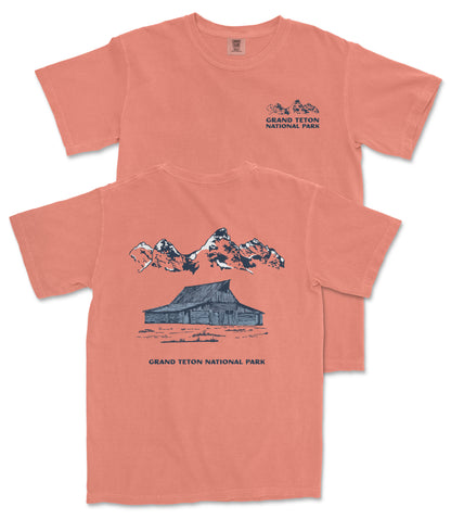 A red t-shirt with a graphic design depicting a cabin and mountains, along with the text "Grand Teton National Park".