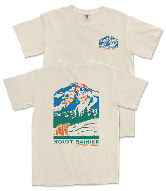 a beige t-shirt with a graphic design depicting a mountain landscape, including a bear and trees. The text on the t-shirt reads "Mount Rainier National Forest" and "National Forest".