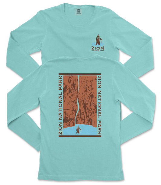 A turquoise long-sleeve t-shirt with a graphic design depicting a person standing in front of a canyon or waterfall.